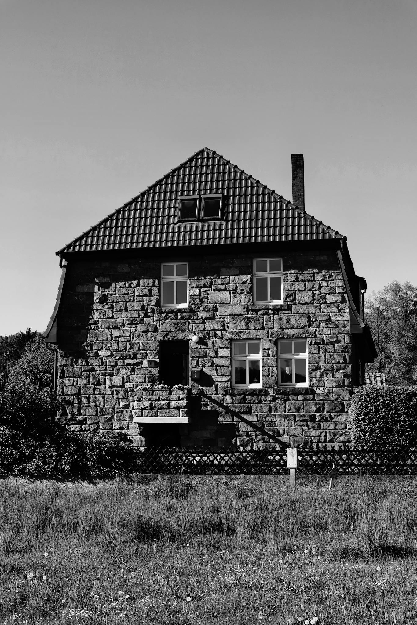 A classic, rustic stone house with a tiled roof captured in dramatic black and white.
