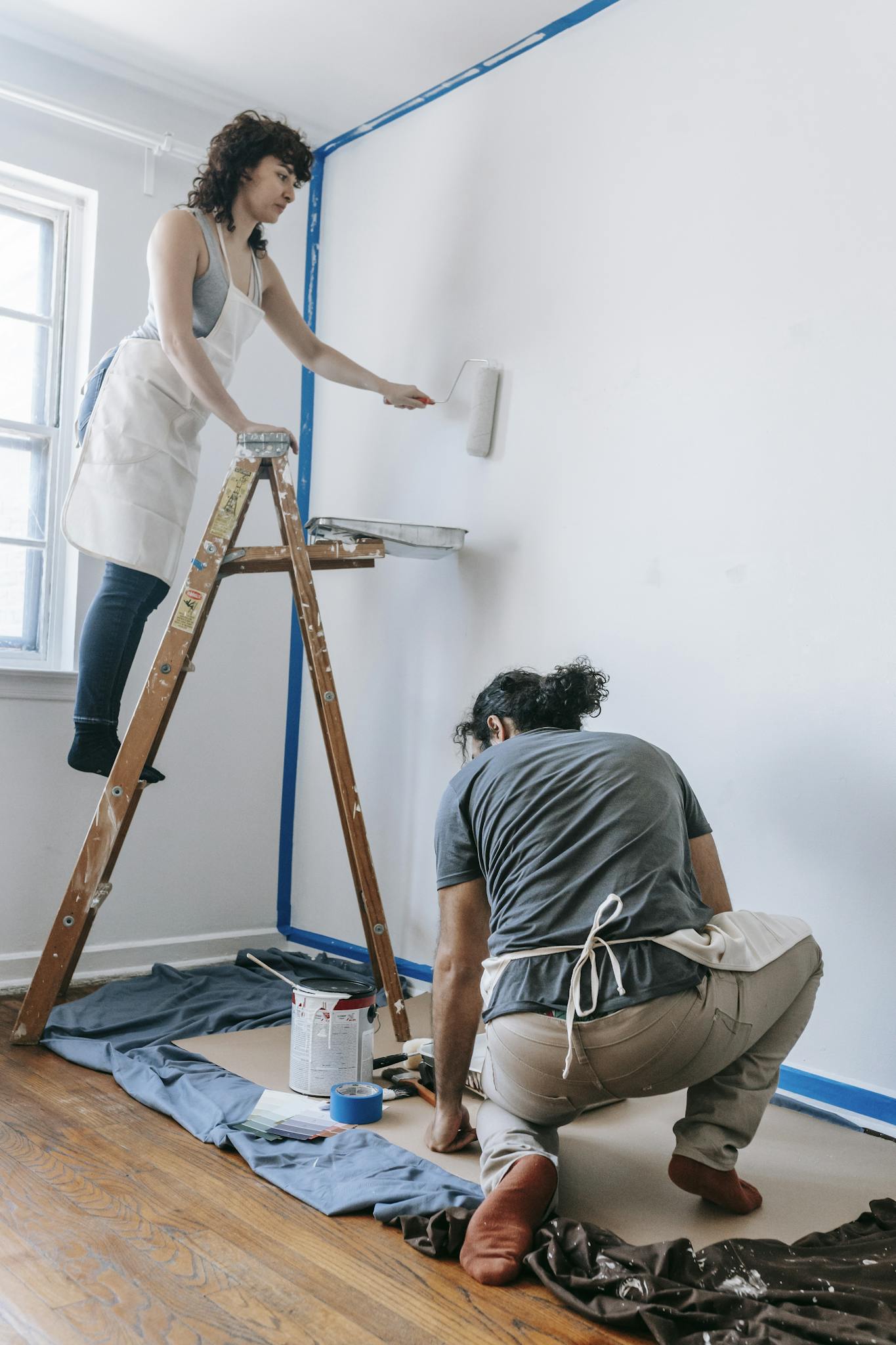 A couple engaged in painting a room with a roller, working together in their new home.