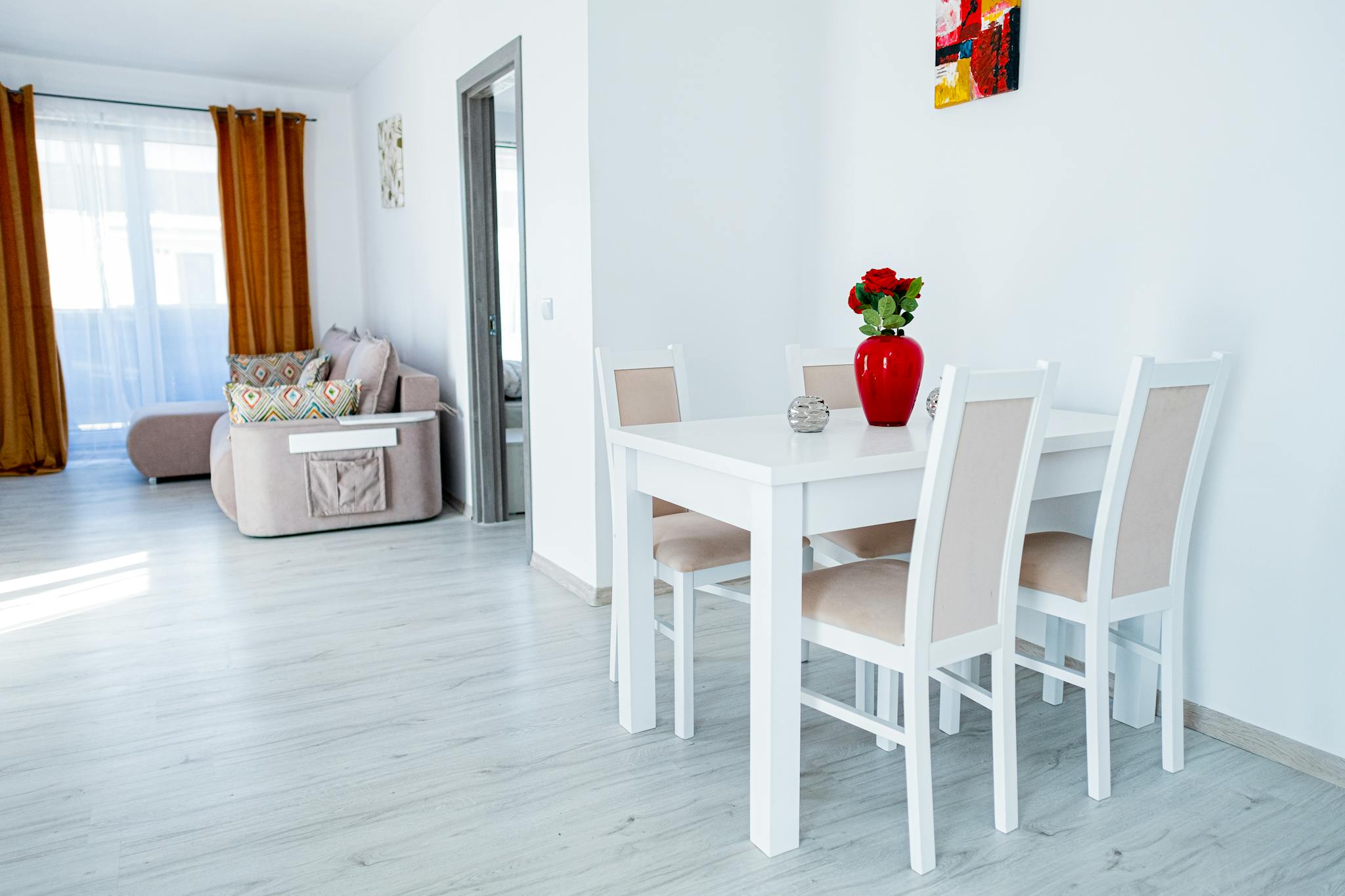 Elegant dining room featuring white furniture, minimalist decor, and natural light streaming in.