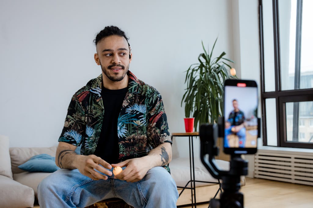 A young man recording video content indoors with a smartphone and tripod.