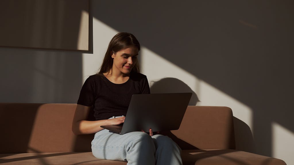 Casual woman enjoying free time browsing laptop on sofa indoors.