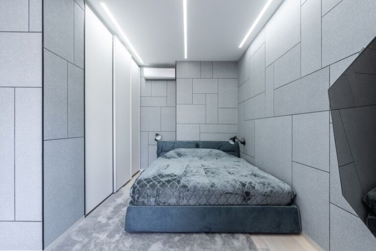 Interior of light modern bedroom with gray bed on carpet near lamps on wall and TV
