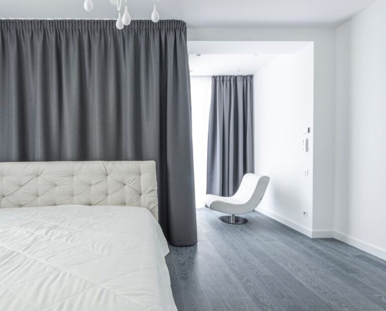 A stylish modern bedroom with white bedding and gray curtains, emphasizing minimalist decor.