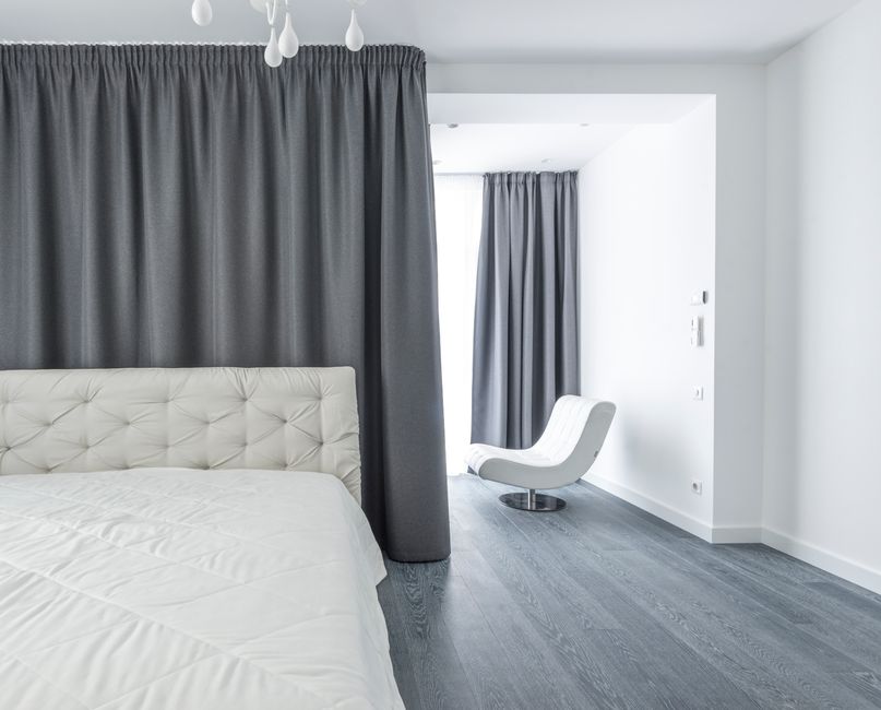 A stylish modern bedroom with white bedding and gray curtains, emphasizing minimalist decor.