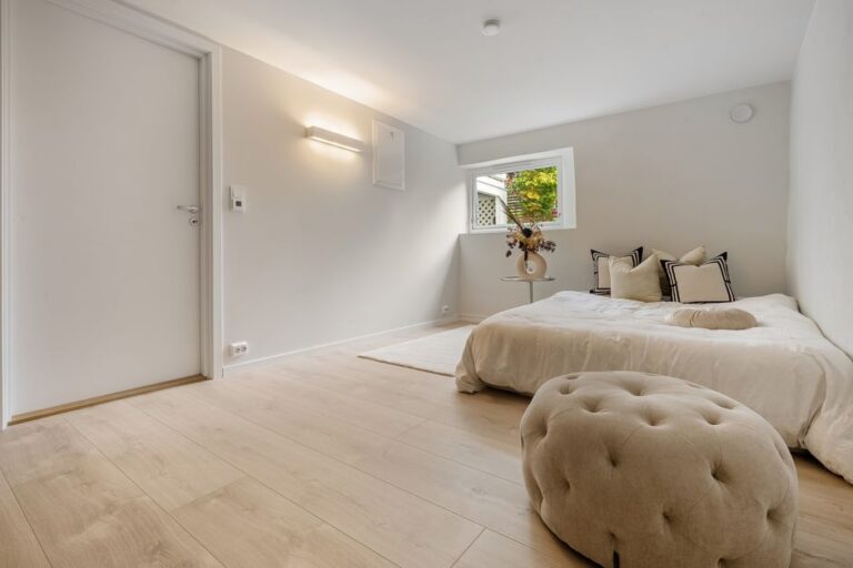A serene bedroom interior with wooden flooring and soft furnishings in natural light.