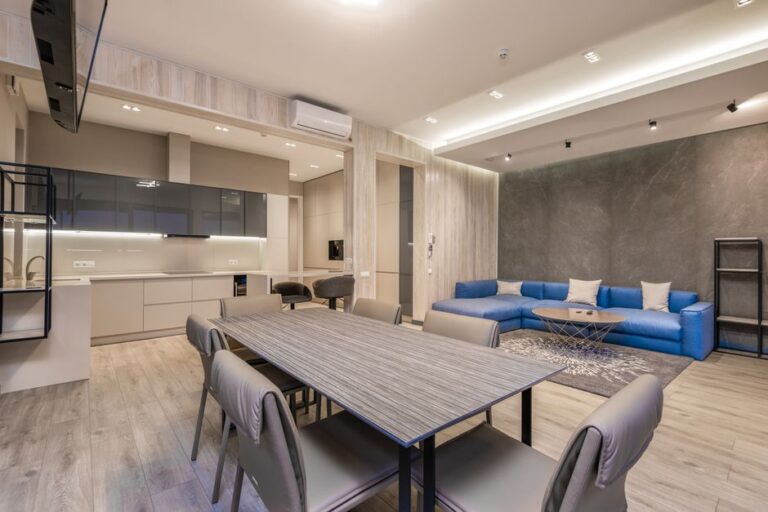 Wooden dining table with chairs placed in spacious living room near kitchen zone in modern apartment