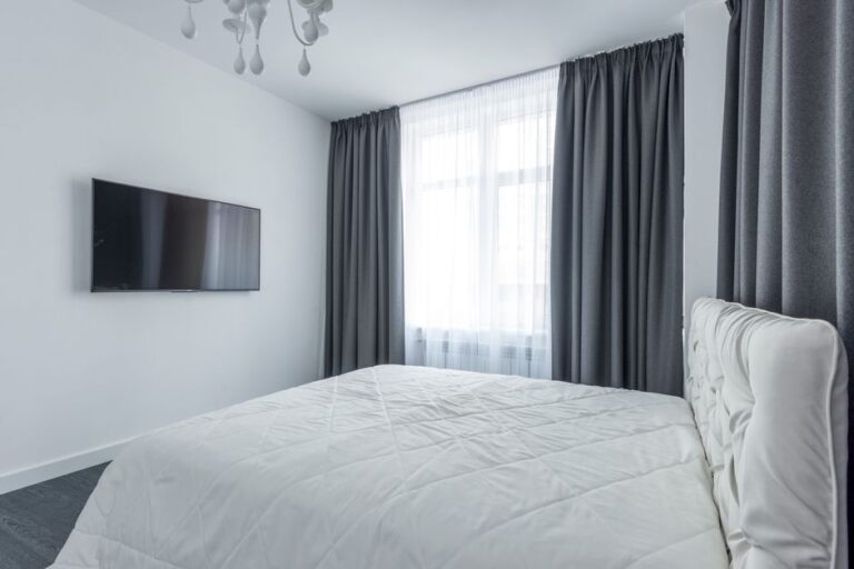 A modern bedroom featuring minimalist decor with a flat-screen TV and elegant curtains.