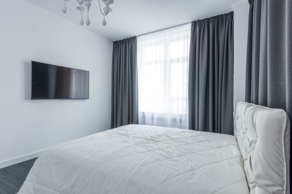 A modern bedroom featuring minimalist decor with a flat-screen TV and elegant curtains.